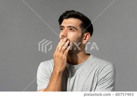 Shocked young Caucasian man looking up and thinking with hand cover mouth  80757403