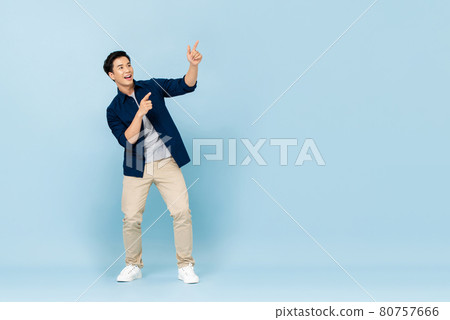Smiling young handsome Asian man pointing fingers to empty space aside 80757666