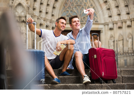 Couple of male tourists with baggage sitting with map at stairs Couple of male tourists with baggage sitting with map at stairs 80757821