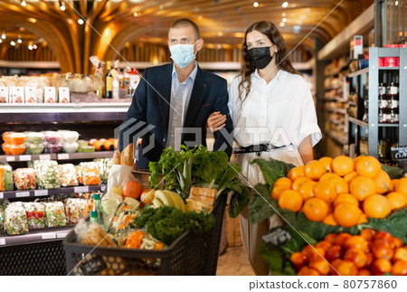 Portrait of a young couple in protective masks walking with a grocery cart through a supermarket 80757860