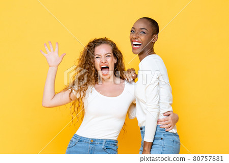 Surprised joyful interracial woman friends looking at camera on isolated yellow studio background Surprised joyful interracial woman friends looking at camera on isolated yellow studio background 80757881