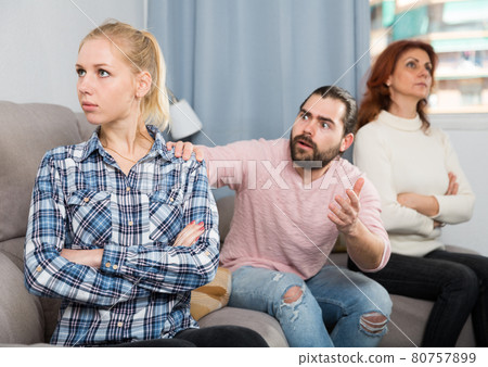 Upset girl sitting after quarrel and man with mother on background Upset girl sitting after quarrel and man with mother on background 80757899