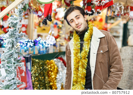 Man with garland choosing decorations at Christmas market Man with garland choosing decorations at Christmas market 80757912