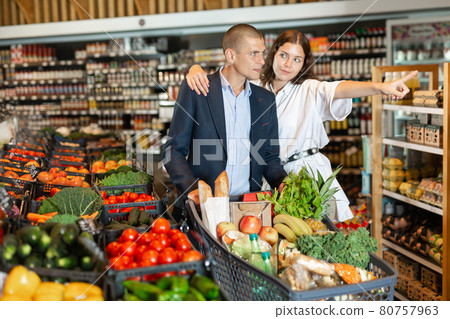 Portrait of a happy young couple in a supermarket with a full grocery cart 80757963