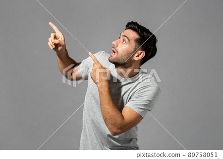 Shocked young Caucasian man gasping with hands pointing up isolated light gray studio background Shocked young Caucasian man gasping with hands pointing up isolated light gray studio background 80758051