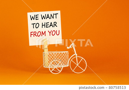 Wooden clothespin with white sheet of paper. Text 'we want to hear from you'. Miniature bicycle model. Beautiful orange background. Business and support concept, copy space. 80758513