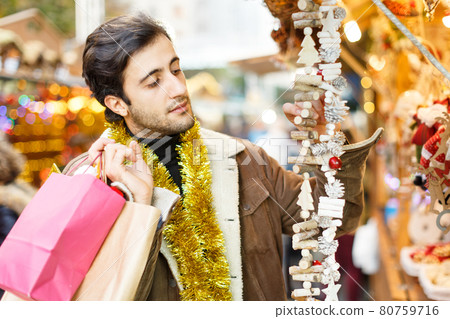Serious young man choosing Christmas toys at fair outdoor 80759716