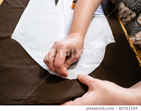 woman fixes paper pattern layout to brown fabric woman fixes paper pattern layout to brown fabric 80761104