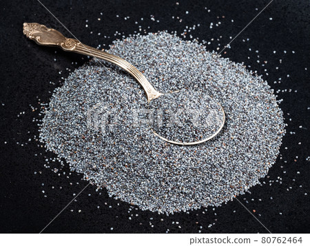 tablespoon in pile of poppy seeds on black plate 80762464