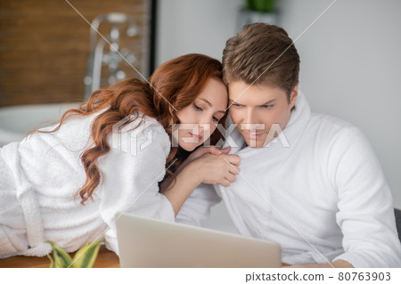 Ginger woman in a white bathrobe and her husband looking happy and in love Ginger woman in a white bathrobe and her husband looking happy and in love 80763903