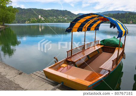 Traditional Pletna boat waiting for tourists on Lake Bled, with the lake island and charming little church in the background, famous tourists attraction in Slovenia 80767181