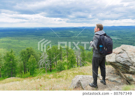 A man in a gray jacket stands on a mountain peak in full growth. A man in a gray jacket stands on a mountain peak in full growth. 80767349