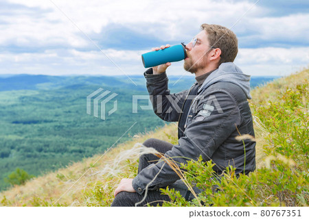 A man in a gray jacket on a mountain top drinks water from a bottle. Close up. A man in a gray jacket on a mountain top drinks water from a bottle. Close up. 80767351