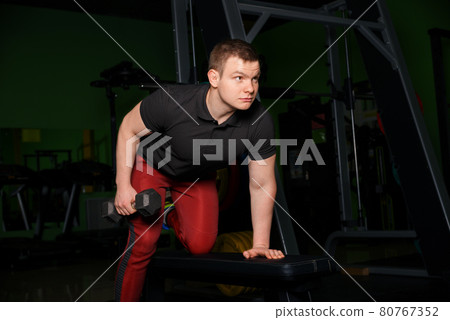 The guy performs a dumbbell pull from the bench. The guy performs a dumbbell pull from the bench. 80767352