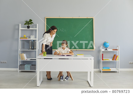 Friendly school teacher helping little pupil with math assignment in modern classroom 80769723