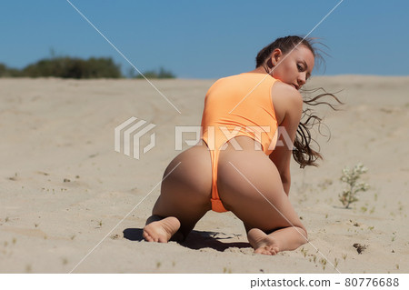 Seductive model in swimsuit kneeling on sandy beach 80776688