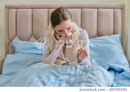 Sick young woman in bed with handkerchief and cup Sick young woman in bed with handkerchief and cup 80780594
