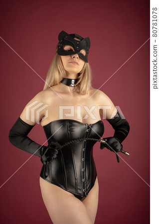 Beautiful young woman in a leather corset and cat mask posing with a whip in her hands Beautiful young woman in a leather corset and cat mask posing with a whip in her hands 80781078