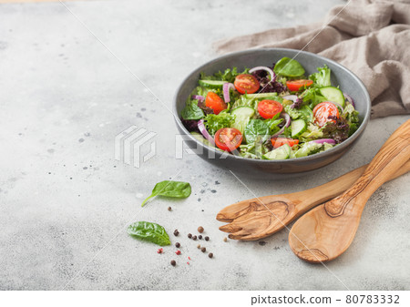 Spatula fork and spoon with bowl of healthy vegetarian vegetables salad with tomatoes and cucumber, lettuce and spinach on light background. Spatula fork and spoon with bowl of healthy vegetarian vegetables salad with tomatoes and cucumber, lettuce and spinach on light background. 80783332