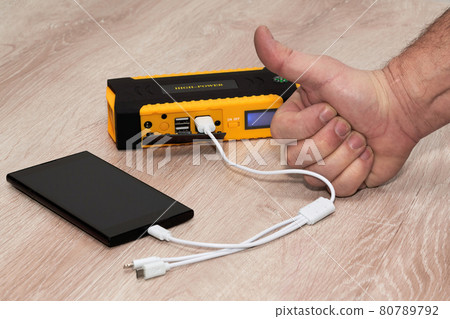 Hand with a raised thumb next to a smartphone charging from a plunging powerbank Hand with a raised thumb next to a smartphone charging from a plunging powerbank 80789792