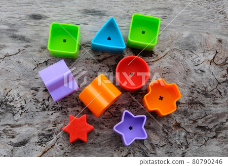 Isolated children's toy blocks in various shapes made of plastic on wood grain background.  80790246