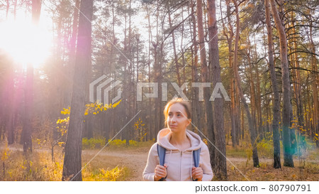 Woman with backpack walking in autumn park, sun lens flares Woman with backpack walking in autumn park, sun lens flares 80790791