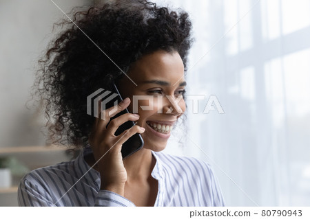 Smiling African American woman look in window talking on smartphone Smiling African American woman look in window talking on smartphone 80790943