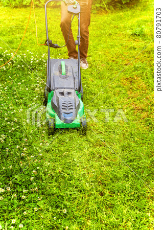 Man cutting green grass with lawn mower in backyard. Gardening country lifestyle background. Beautiful view on fresh green grass lawn in sunlight, garden landscape in spring or summer season. 80791703