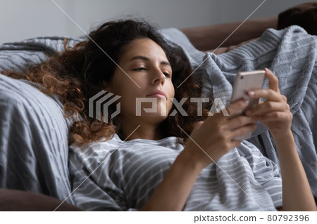 Lazy indifferent woman resting in bed, using smartphone Lazy indifferent woman resting in bed, using smartphone 80792396