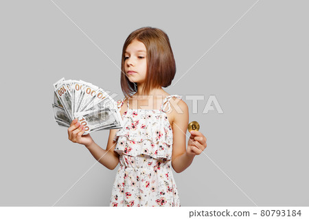 Beautiful little girl holding virtual currency bitcoin and dollars perplexedly don't know what to choose to invest future 80793184