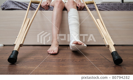 Woman with broken leg sitting on the bed and holding crutches. High quality photo 80794282