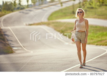 Graceful blond woman walks on empty road. Graceful blond woman walks on empty road. 80797027