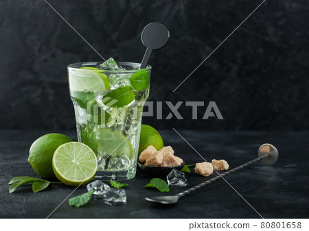 Glass of Mojito cocktail with ice cubes mint and lime on black board with spoon and fresh limes  80801658