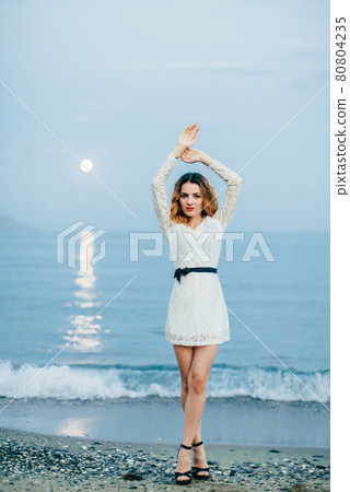Caucasian girl posing by the sea on the beach in the evening Caucasian girl posing by the sea on the beach in the evening 80804235