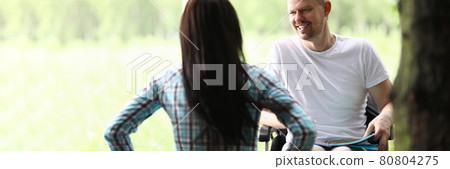 Man in wheelchair in park communicates with woman 80804275