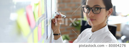 Businesswoman with glasses stands near blackboard with marker Businesswoman with glasses stands near blackboard with marker 80804276