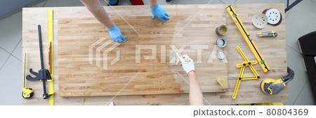Two craftsmen are covering wooden table with protective varnish Two craftsmen are covering wooden table with protective varnish 80804369