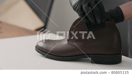 man hands in black gloves applying protective cream to brown leather chukka boots 80805135