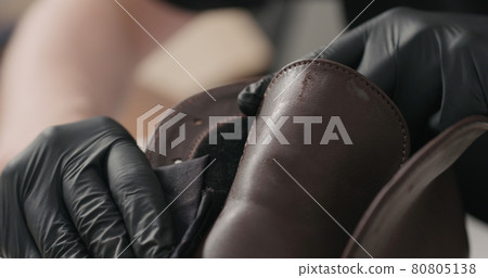 man hands in black gloves applying protective cream to brown leather chukka boots 80805138