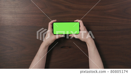 Top view man hand hold smartphone with green screen over black walnut wood table Top view man hand hold smartphone with green screen over black walnut wood table 80805174