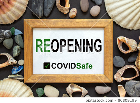 Wooden picture frame with inscription 'reopening covidsafe' on beautiful black background. Sea stones and seashells. Concept. Wooden picture frame with inscription 'reopening covidsafe' on beautiful black background. Sea stones and seashells. Concept. 80809199