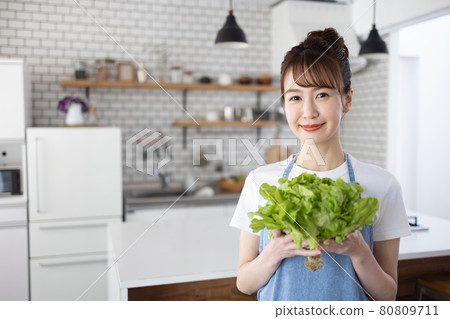 Woman in an apron holding vegetables in the kitchen Woman in an apron holding vegetables in the kitchen 80809711