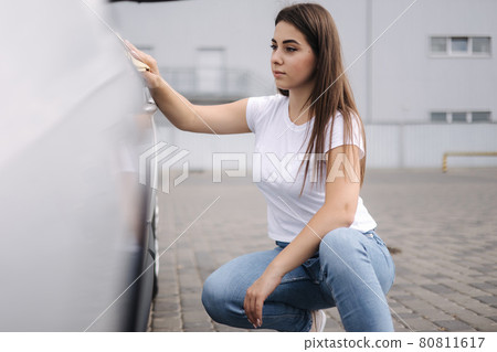 Front view of attractive happy joyful female driver washing her car with special rag in self-service car wash 80811617