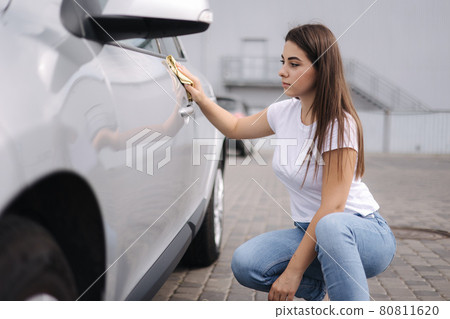 Attractive happy joyful female driver wipe her car using rag in self-service car wash 80811620