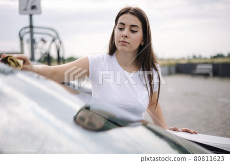 Attractive happy joyful female driver wipe windshield on her car using rag in self-service car wash Attractive happy joyful female driver wipe windshield on her car using rag in self-service car wash 80811623