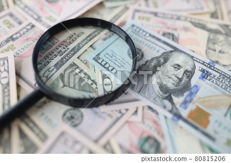 One hundred dollar bills and magnifying glass lie on table closeup One hundred dollar bills and magnifying glass lie on table closeup 80815206