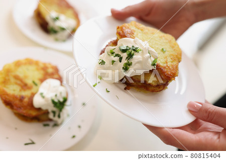 Woman holds plate with potato pancakes and sour cream and herbs in hands 80815404