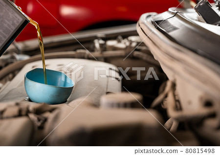 Auto mechanic pours oil into a car engine. Auto mechanic pours oil into a car engine. 80815498