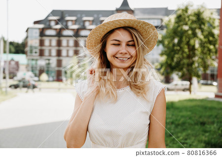 A beautiful blonde walks through a city. Woman in white dress and straw hat A beautiful blonde walks through a city. Woman in white dress and straw hat 80816366