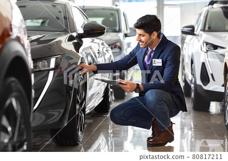 Handsome man in suit sales assistant checking car tires Handsome man in suit sales assistant checking car tires 80817211